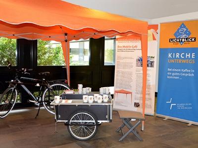 Ein Fahrrad mitsamt Anhänger, Sonnenpavillion, Hockern und Café-Ausrüstung