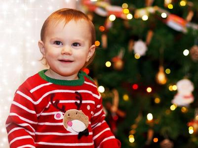 lachendes Kleinkind vor einem geschmückten Weihnachtsbaum