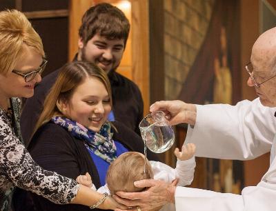 Priester und eine Familie mit Kleinkind am Taufbecken