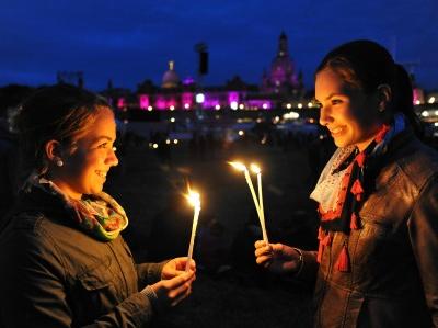 zwei junge Frauen mit brennenden Kerzen vor der nächtlichen Skyline von Dresden