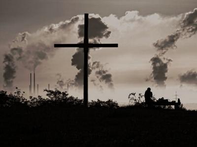 qualmende Industrieschornsteine, im Vordergrund ein Kreuz.