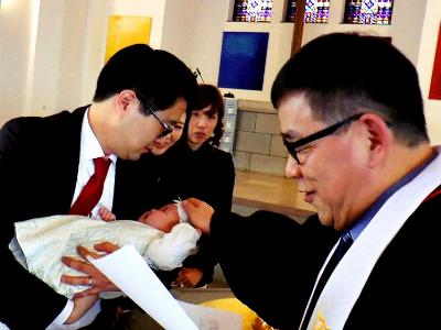 Pfarrer und Elternpaar taufen ein Kind