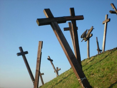 mehrere große Holzkreuze stehen ungeordnet auf einem grünen Hügel