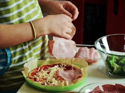 Kinderhände belegen eine Pizza mit Zutaten