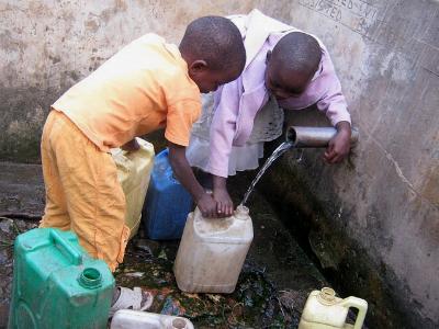 zwei afrikanische Kinder mit Wasserkanistern an einem Brunnen