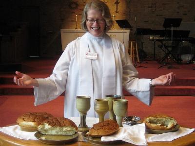 Pfarrerin im weißen Ornat vor einem Altar mit Abendmahl