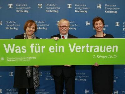 Kirchenvertreter halten Schild mit der Kirchentagslosung für 2019 'Was für ein Vertrauen'