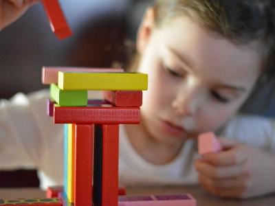 Kind mit wackeligem Turm aus Bauklötzen