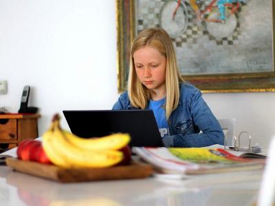 Mädchen mit Laptop macht am Küchentisch Hausaufgaben