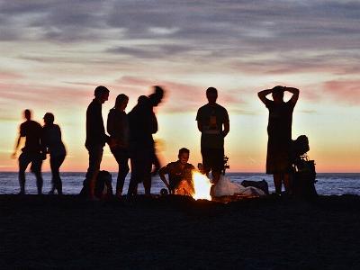 Jugendliche im Abendlicht stehen um ein Lagerfeuer