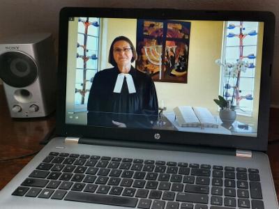 Laptop-Bildschirm zeigt Pfarrerin beim Online-Gottesdienst