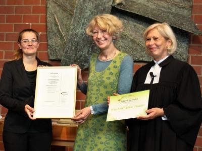 eine Pfarrerin und zwei weitere Frauen präsentieren stolz eine Urkunde