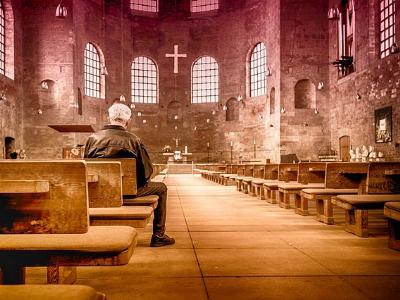 älterer Mann sitzt alleine in einer großen Kirche
