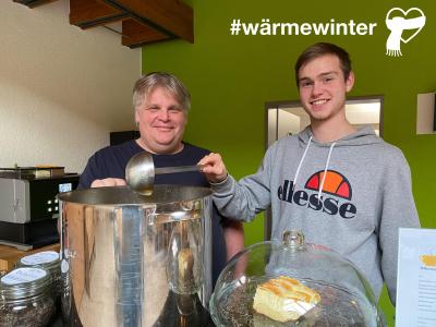 zwei Männer hinter einem großen Kochtopf mit Suppe