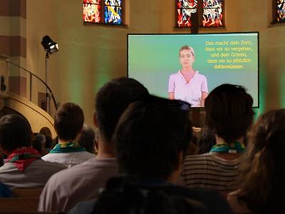 Kirchentagsbesucher schauen auf eine Videoleinwand