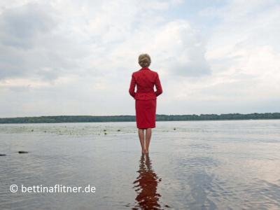 Frau in rotem Kosrüm steht barfuß im flachen Wasser