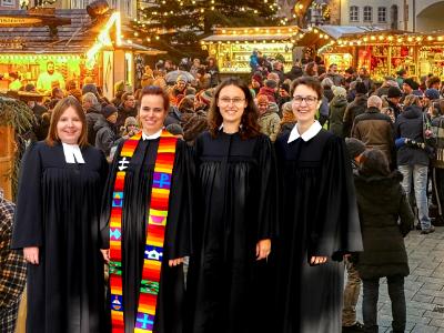 vier Pfarrerinnen im Talar auf einem Weihnachtsmarkt